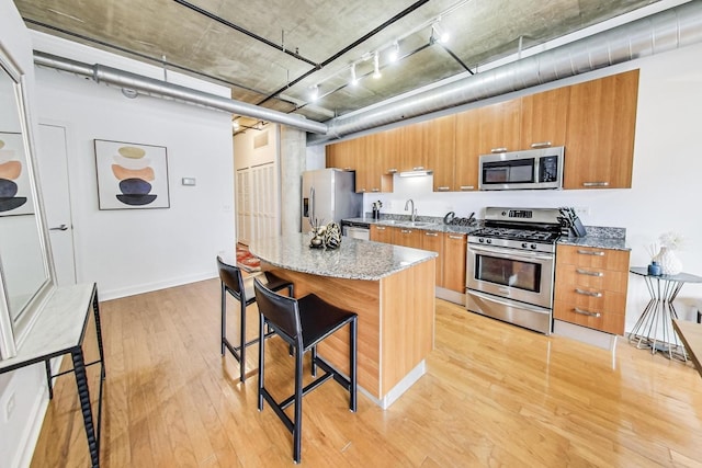 kitchen with a breakfast bar area, brown cabinetry, stainless steel appliances, light wood-type flooring, and a center island