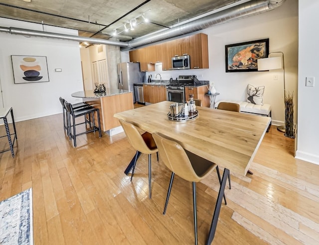 dining space featuring rail lighting, baseboards, and light wood-style floors