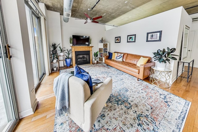 living area with light wood finished floors, a glass covered fireplace, and a ceiling fan