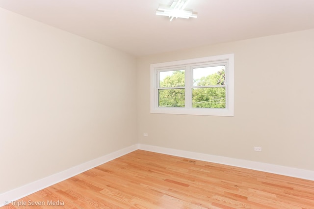 empty room with baseboards, visible vents, and light wood finished floors