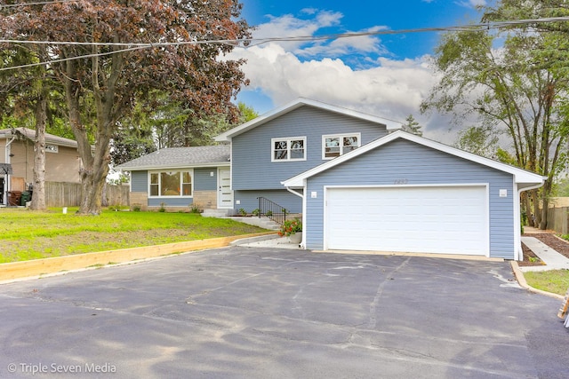 split level home featuring driveway, a front lawn, an attached garage, and fence