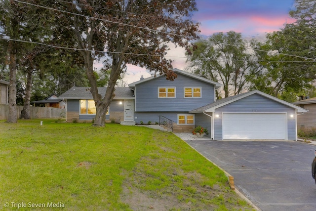 split level home with aphalt driveway, a lawn, an attached garage, entry steps, and fence