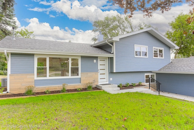 tri-level home with entry steps, stone siding, roof with shingles, a front lawn, and a chimney