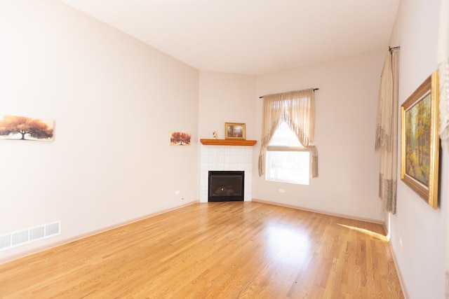 unfurnished living room featuring light wood-style floors, baseboards, visible vents, and a tile fireplace