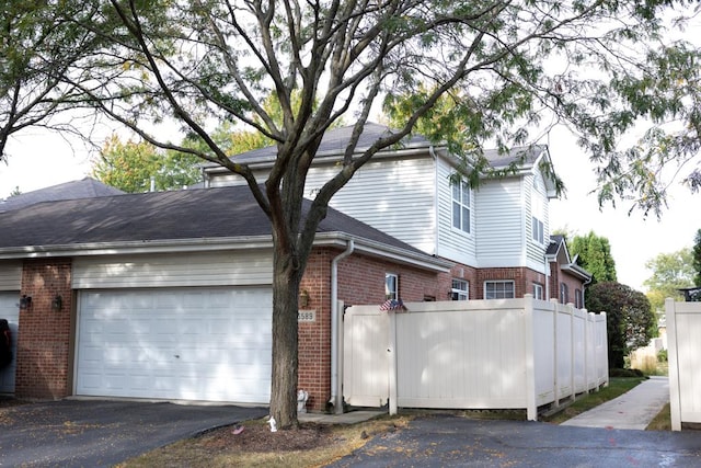 view of home's exterior featuring aphalt driveway, an attached garage, brick siding, fence, and roof with shingles