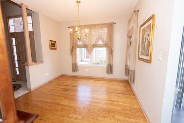 unfurnished dining area with light wood-style floors, a chandelier, decorative columns, and baseboards