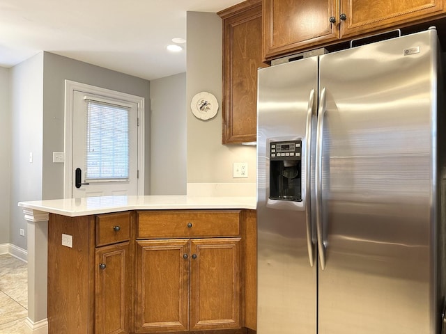 kitchen with baseboards, stainless steel fridge, a peninsula, light countertops, and brown cabinets