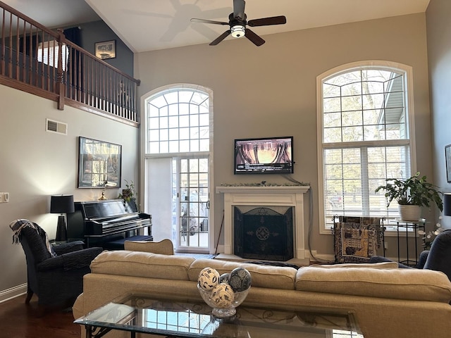 living room featuring visible vents, baseboards, a fireplace with raised hearth, ceiling fan, and wood finished floors
