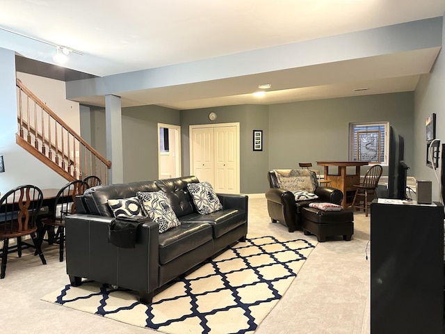 living area with light carpet, stairs, and rail lighting