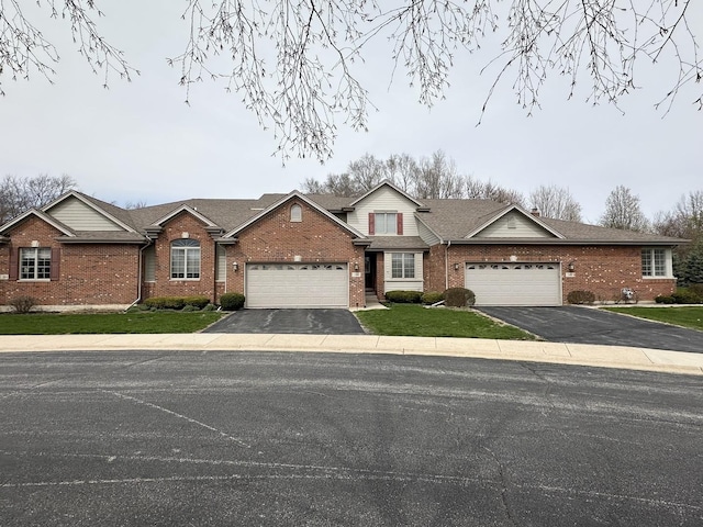 view of front of home with an attached garage, aphalt driveway, a front lawn, and brick siding