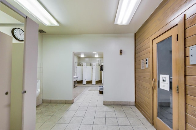 hall with light tile patterned floors, wood walls, and baseboards