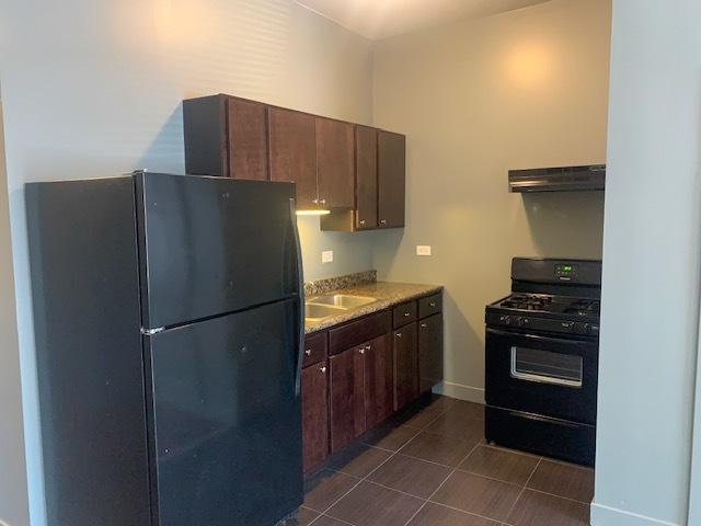 kitchen featuring light countertops, a sink, dark tile patterned flooring, under cabinet range hood, and black appliances