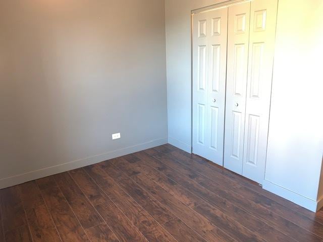 unfurnished bedroom featuring a closet, dark wood finished floors, and baseboards