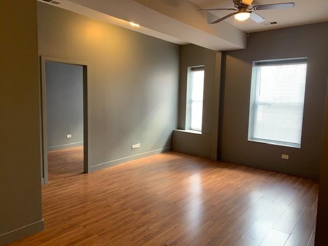 unfurnished room featuring a healthy amount of sunlight, visible vents, baseboards, and wood finished floors