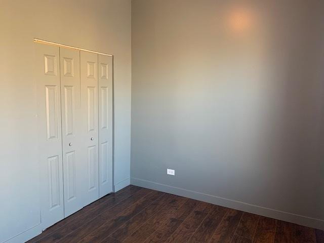 unfurnished bedroom featuring dark wood-type flooring, a closet, and baseboards