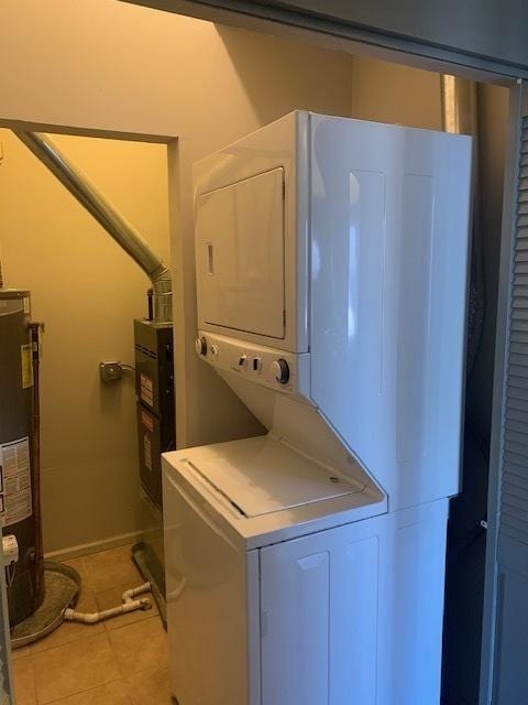 laundry area with light tile patterned flooring, laundry area, stacked washer and dryer, baseboards, and water heater