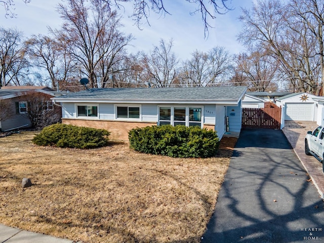 ranch-style house with brick siding, fence, aphalt driveway, an outbuilding, and a gate