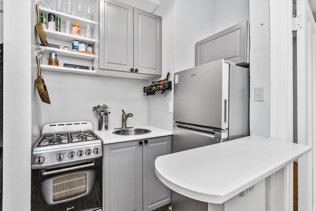 kitchen featuring appliances with stainless steel finishes, a peninsula, light countertops, gray cabinetry, and a sink