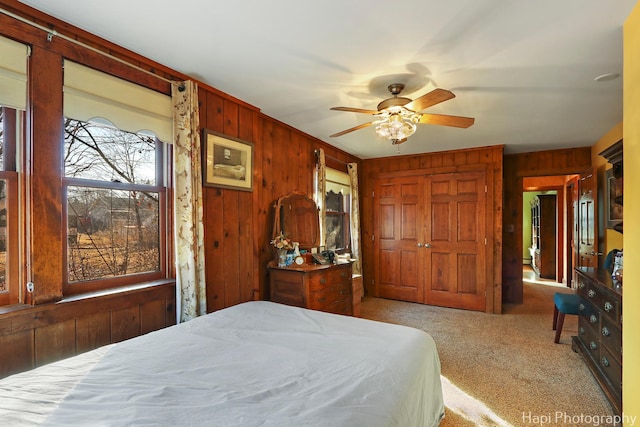 carpeted bedroom with wood walls, a closet, and a ceiling fan