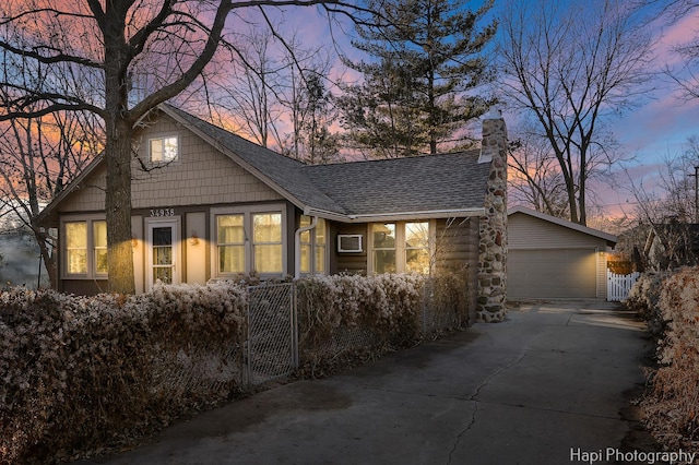 view of front of home featuring a shingled roof, fence, a chimney, and a detached garage