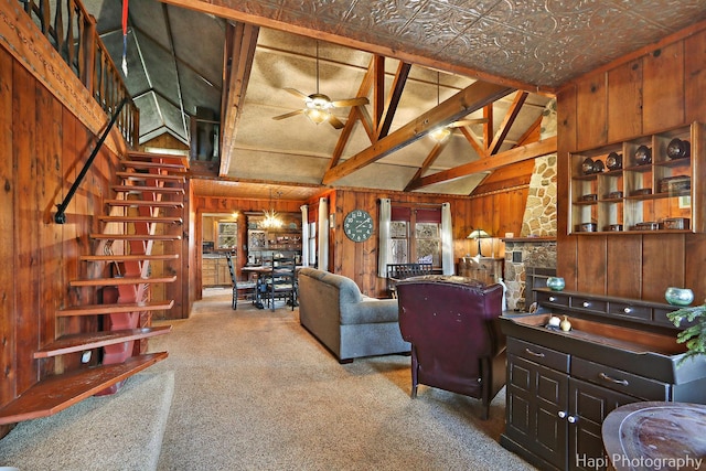 carpeted living room featuring wood walls, a ceiling fan, vaulted ceiling, stairway, and an ornate ceiling