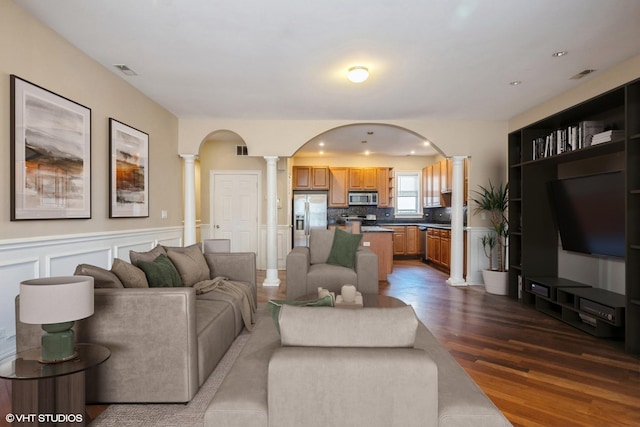 living area with visible vents, dark wood-type flooring, decorative columns, wainscoting, and arched walkways