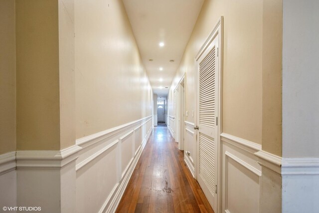 corridor featuring a decorative wall, recessed lighting, a wainscoted wall, and wood-type flooring