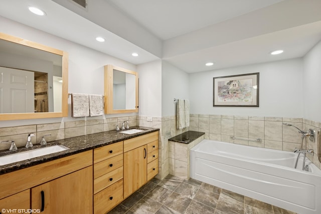 bathroom featuring a garden tub, recessed lighting, double vanity, and a sink