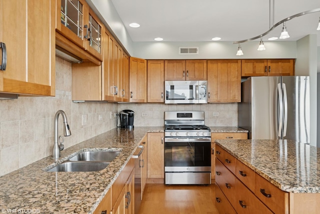 kitchen featuring visible vents, a sink, appliances with stainless steel finishes, brown cabinets, and backsplash