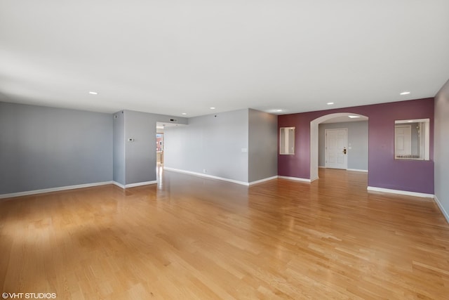 spare room featuring arched walkways, recessed lighting, light wood-type flooring, and baseboards