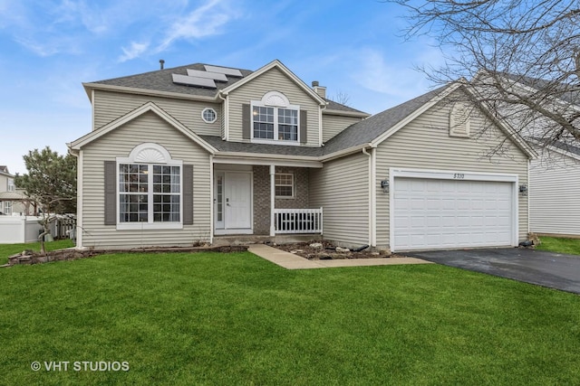 traditional home featuring aphalt driveway, an attached garage, covered porch, roof mounted solar panels, and a front lawn