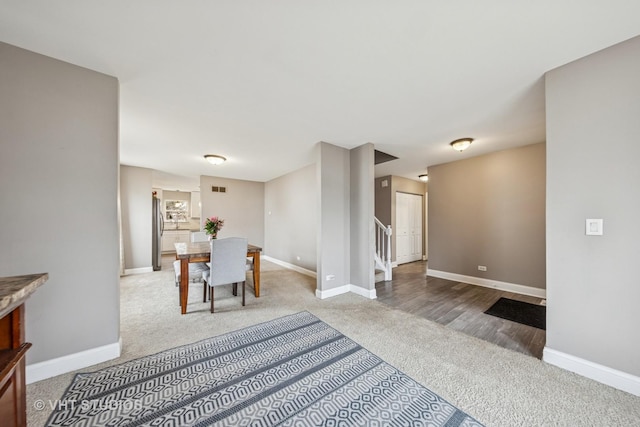 carpeted dining room with stairway, visible vents, and baseboards