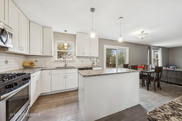 kitchen with stainless steel appliances, decorative backsplash, a sink, and light wood-style floors