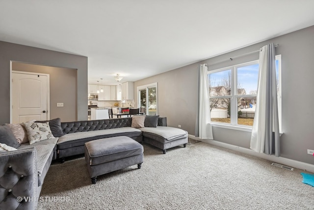 living area featuring baseboards, light carpet, visible vents, and a healthy amount of sunlight