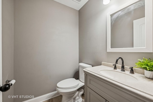 half bath featuring baseboards, vanity, and toilet