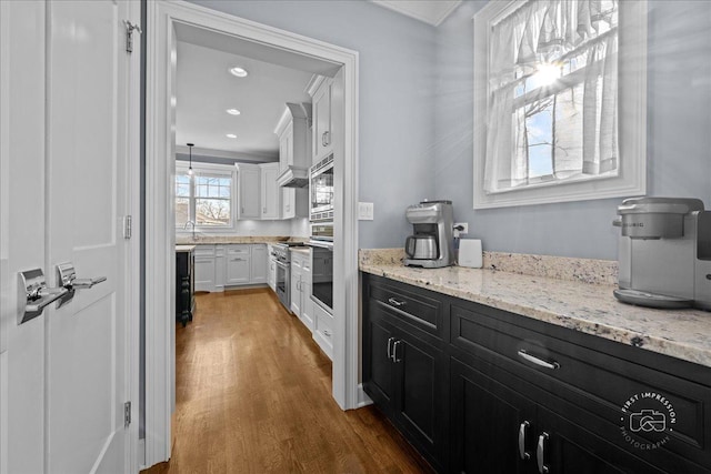 kitchen featuring stainless steel appliances, dark cabinetry, wood finished floors, white cabinetry, and a sink