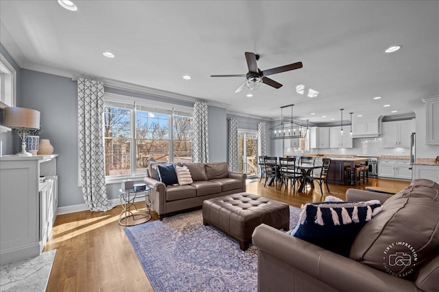 living area featuring baseboards, ornamental molding, recessed lighting, light wood-style flooring, and a ceiling fan