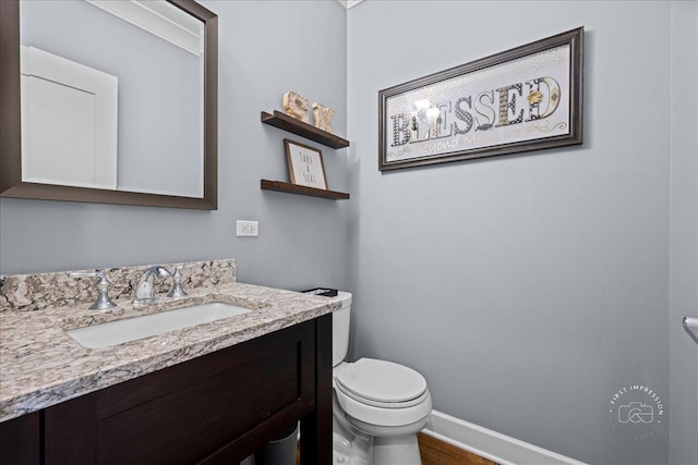 half bathroom featuring vanity, toilet, and baseboards