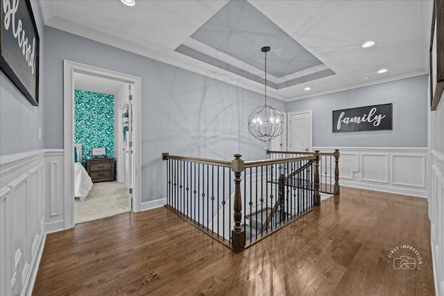 corridor with a notable chandelier, a decorative wall, a raised ceiling, and wood finished floors