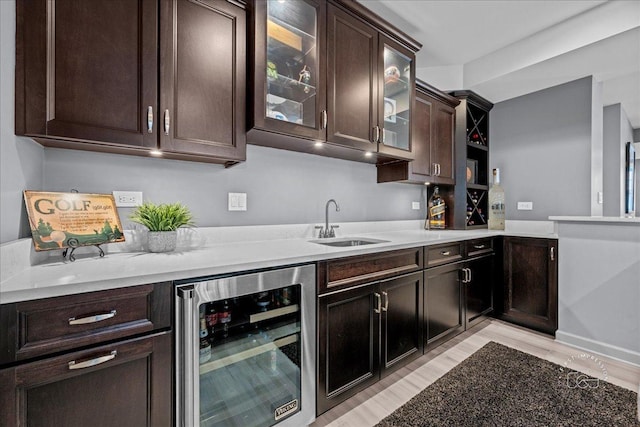 kitchen featuring beverage cooler, a sink, light countertops, glass insert cabinets, and dark brown cabinets