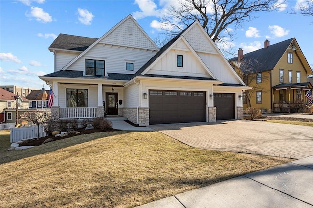 view of front facade featuring a front lawn, decorative driveway, stone siding, board and batten siding, and covered porch