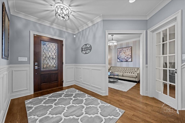 entrance foyer featuring a wainscoted wall, a notable chandelier, wood finished floors, and ornamental molding