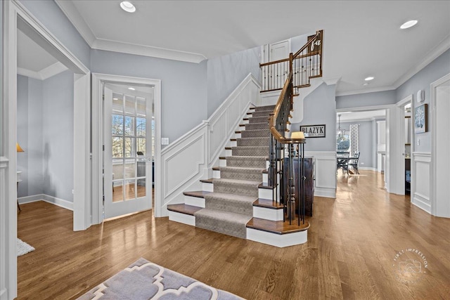 foyer entrance with stairs, crown molding, a decorative wall, and wood finished floors