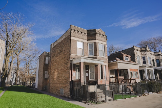 multi unit property with brick siding, a front lawn, and fence