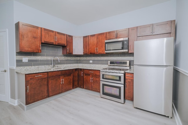 kitchen featuring stainless steel appliances, backsplash, a sink, and light stone countertops