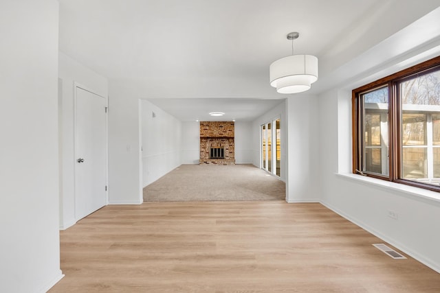 unfurnished living room with light wood-type flooring, visible vents, light carpet, a large fireplace, and baseboards