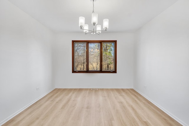 spare room with light wood-type flooring, baseboards, and a notable chandelier