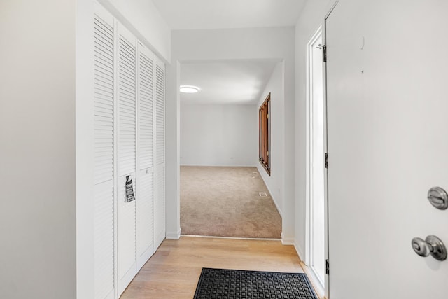 hallway with baseboards, light wood-style floors, and light carpet