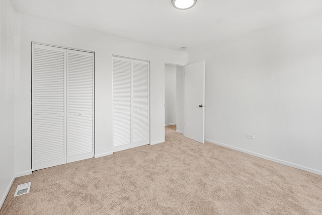 unfurnished bedroom with visible vents, carpet flooring, two closets, and baseboards