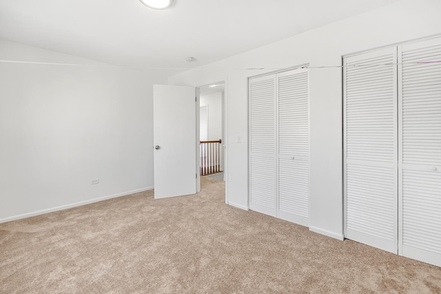 unfurnished bedroom featuring light colored carpet, baseboards, and multiple closets